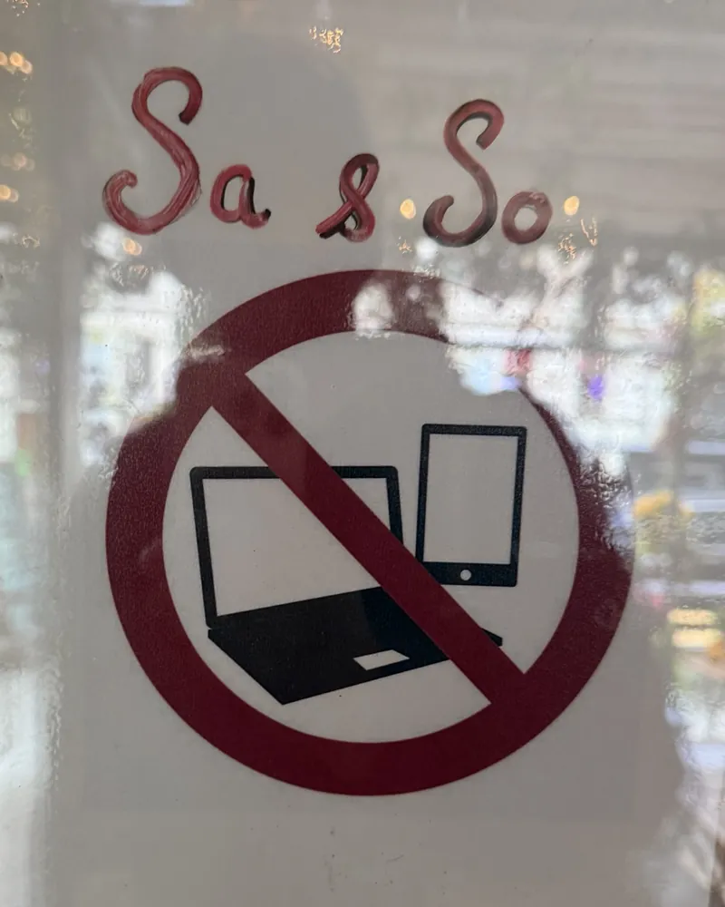 Schild an einer Café-Tür in Berlin: „Sa & So“ von Hand über einem durchgestrichenen Laptop und Tablet